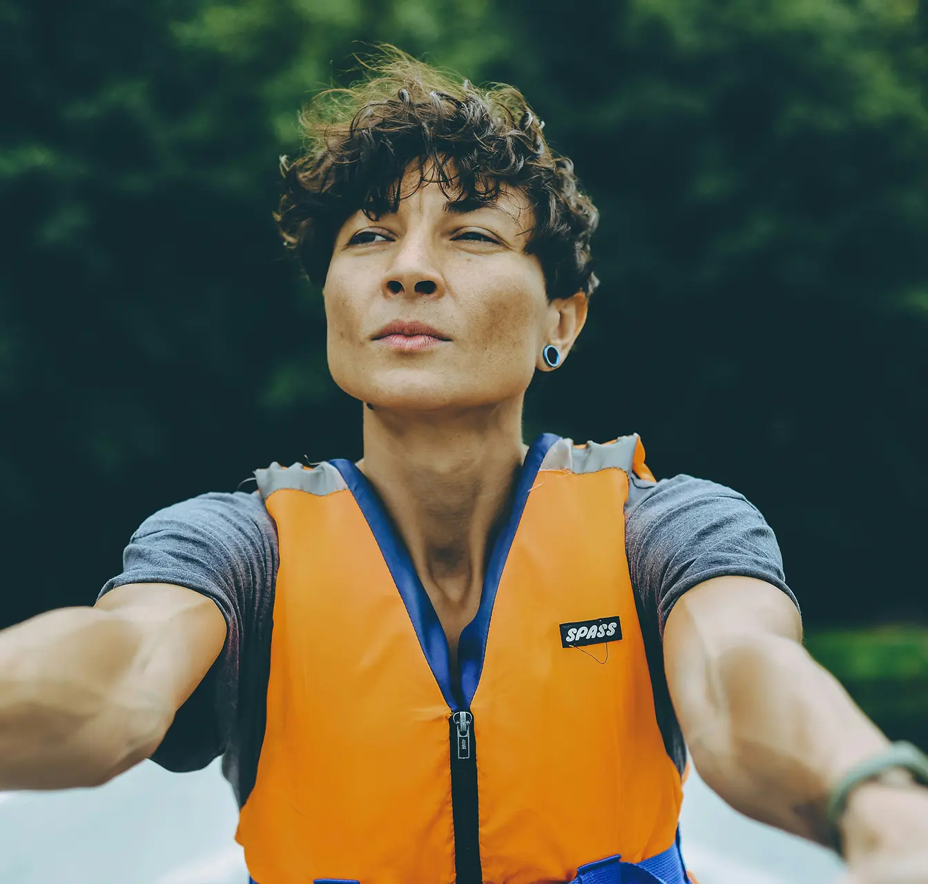 Person with short curly hair wearing an orange life jacket, looking determined with arms extended forward.