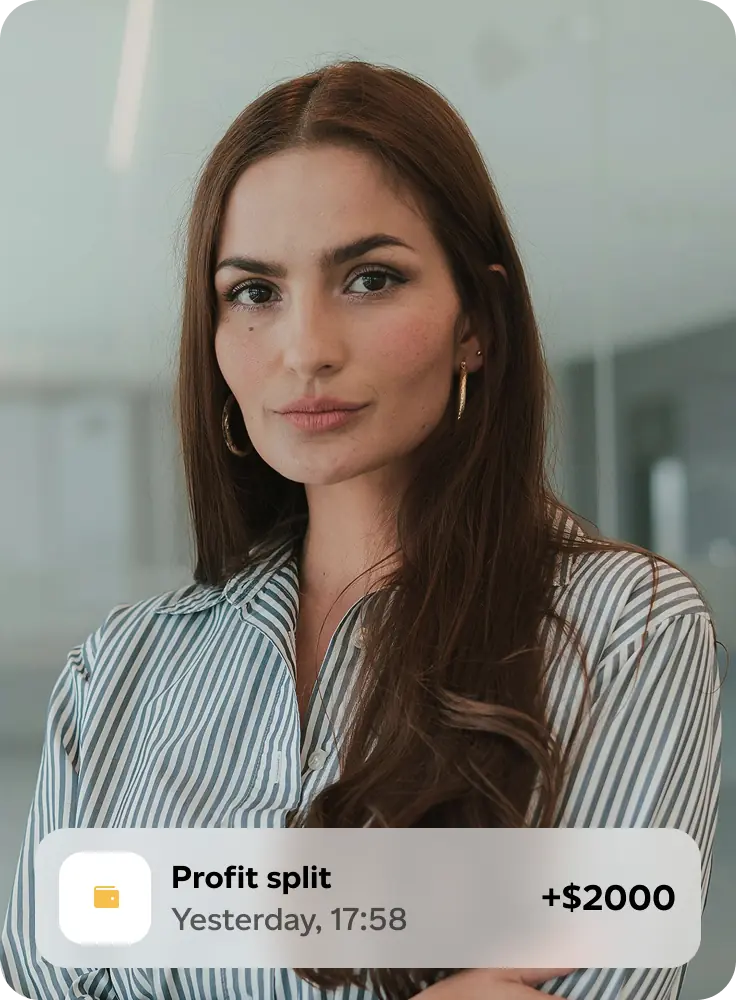 Confident woman with long brown hair and striped shirt stands with arms crossed, overlay shows profit split notification of +$2000.