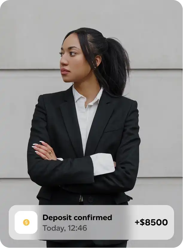 Confident woman in a black suit with arms crossed and a notification overlay showing a confirmed deposit of $8500.
