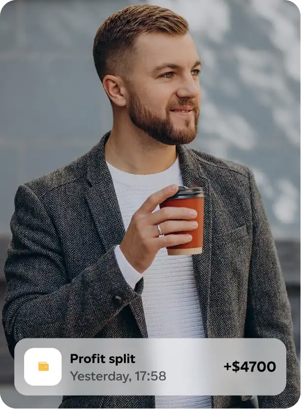 Smiling man in a gray patterned blazer and white sweater holding a takeaway coffee cup, with a popup notification showing a $4700 profit split received yesterday at 17:58.