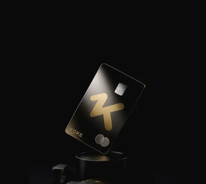 Black and gold Kore credit card standing upright on a black pedestal against a dark background.