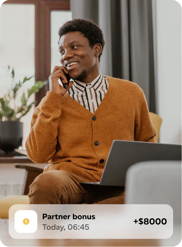 Smiling man holding a phone to his ear and working on a laptop, with a digital notification of an $8000 partner bonus displayed.