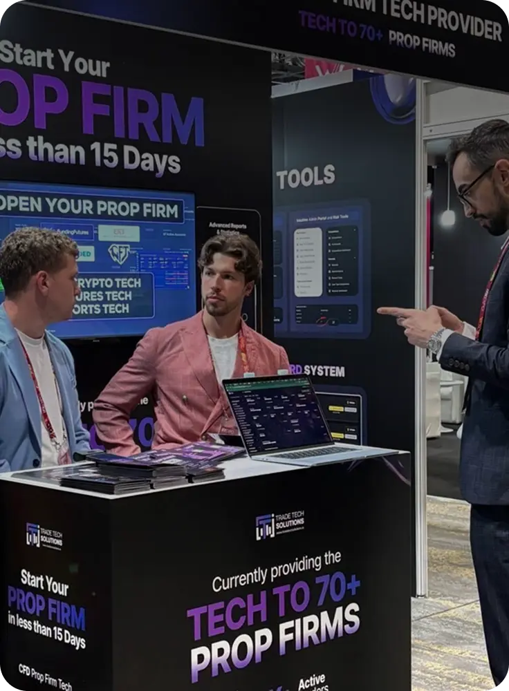 Three men discussing at a Trade Tech Solutions booth with promotional banners about starting a prop firm and technology for over 70 prop firms.