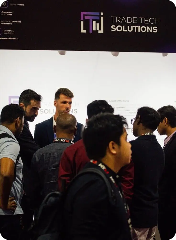 Group of people gathered around a booth with Trade Tech Solutions branding at an event.