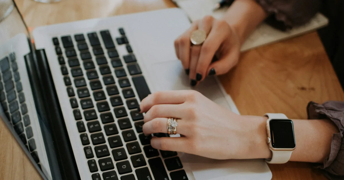 Woman's hands typing on laptop keyboard with rings and Apple Watch — best futures paper trading platform