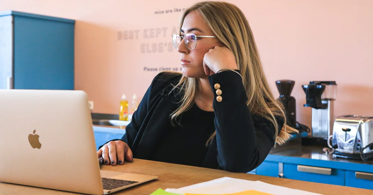 Young woman thoughtfully working on MacBook in modern cafe — how to get into prop trading