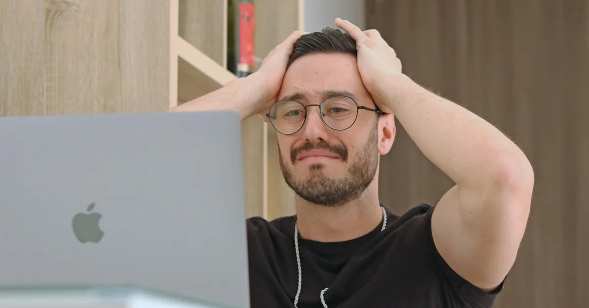 Frustrated man holding head in hands in front of MacBook — what happens if you lose money on a funded account