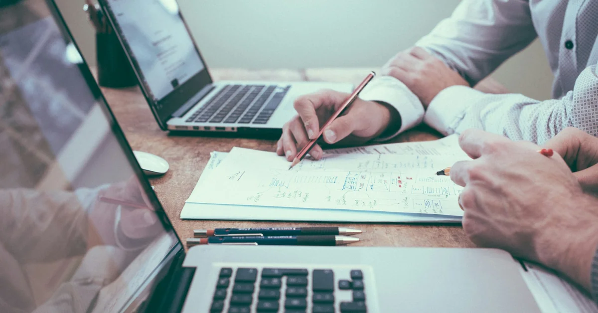 Two people analyzing financial charts and documents on laptops — are funded trading accounts legit