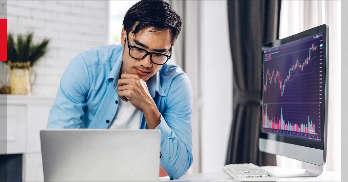 Asian man in blue shirt analyzing stock candlestick chart on monitor — best paper trading simulator