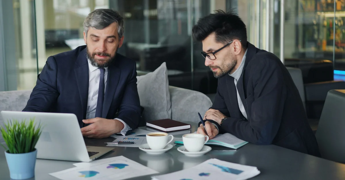 Two businessmen reviewing financial charts on laptop with documents and coffee — what is a prop firm challenge