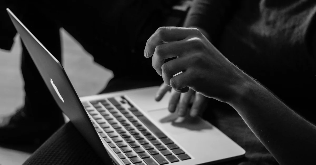 Hands typing on MacBook laptop in black and white — best simulated trading platform