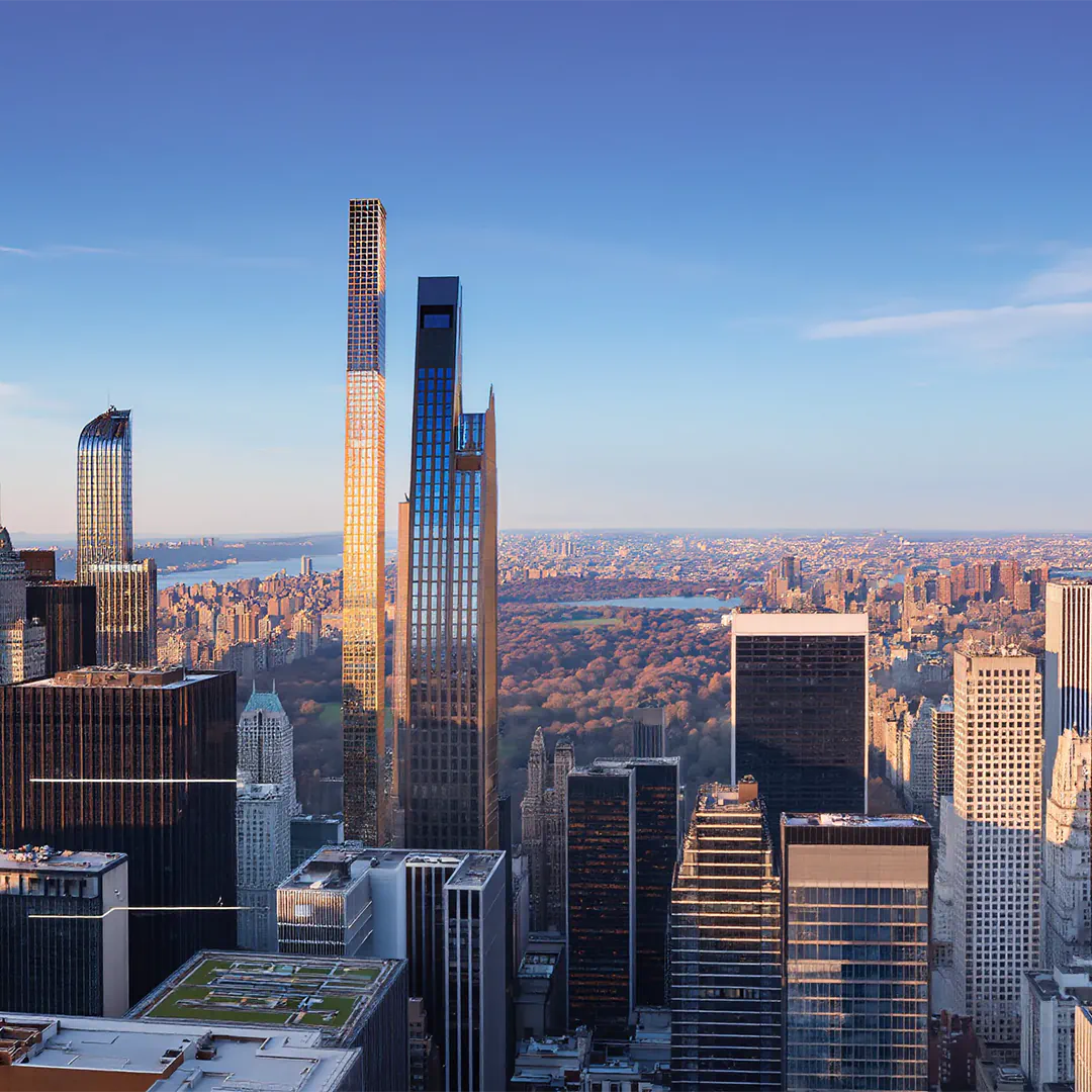 Tall modern skyscrapers overlooking Central Park in New York City under a clear blue sky at sunset.