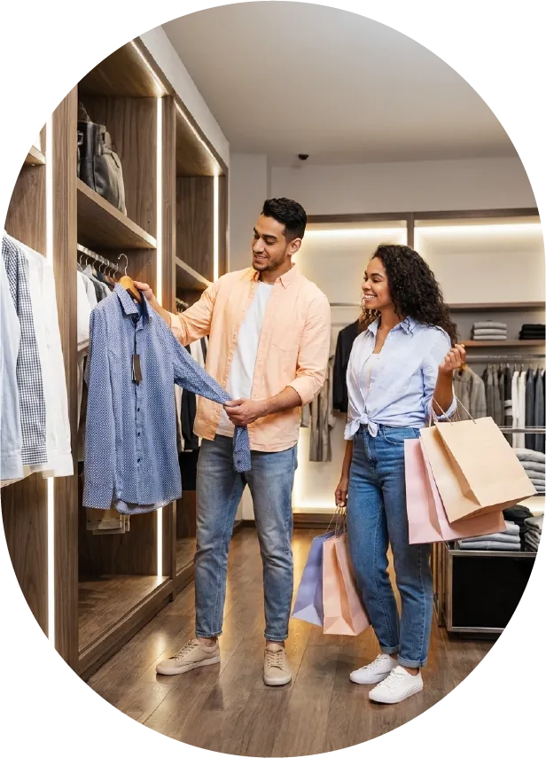 Man holding a blue shirt on a hanger while woman with curly hair holds shopping bags in a clothing store.
