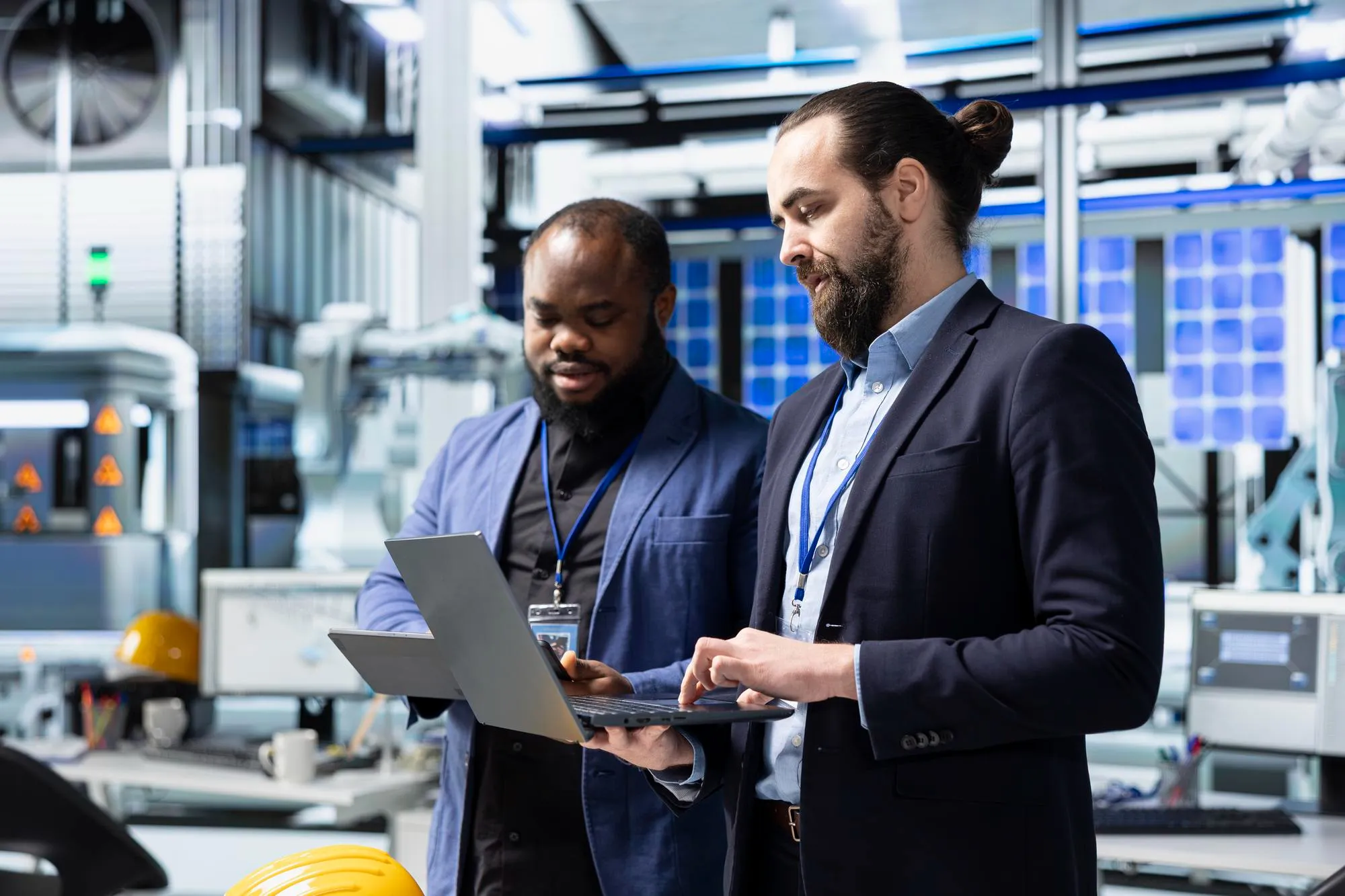 Two engineers in suits looking at a laptop in an industrial technology workspace.
