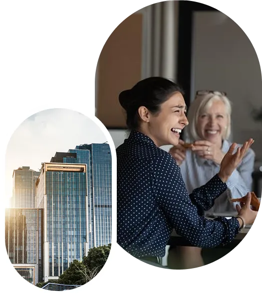 Two women smiling and talking while sharing a meal at a table indoors, with a city skyscraper inset image.