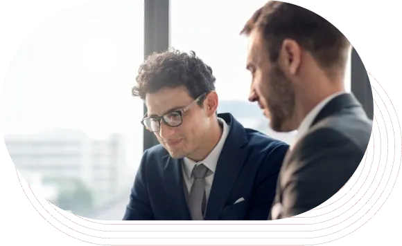 Two businessmen in suits reviewing documents together in an office with a window view.