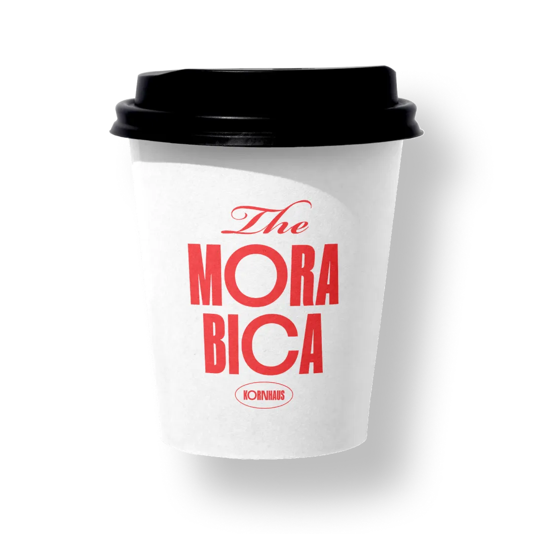 White disposable coffee cup with black lid displaying red text 'The Morabica' and 'Kornhaus' logo.