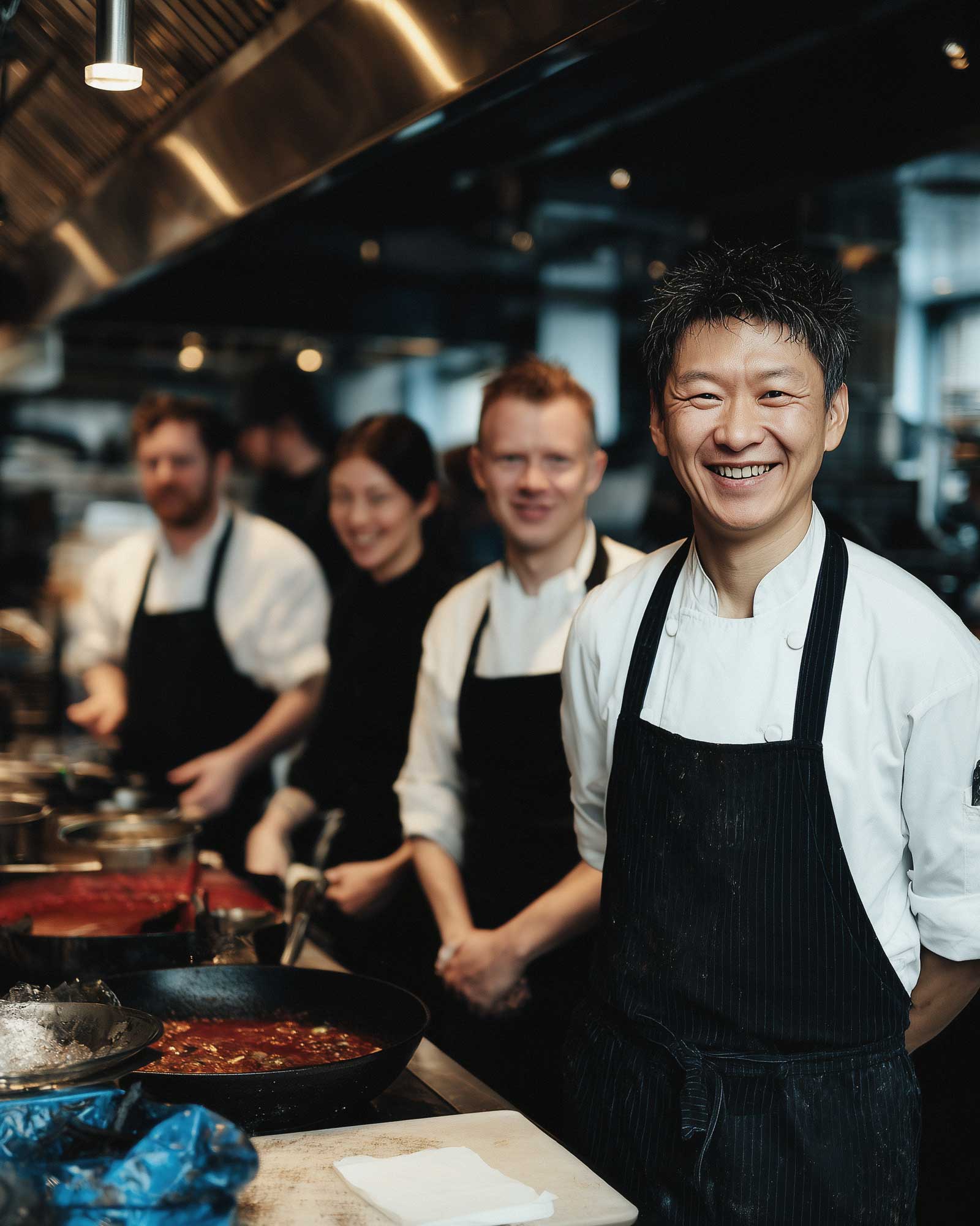 Chef smiling at the camera with the kitchen team standing behind in a professional workspace