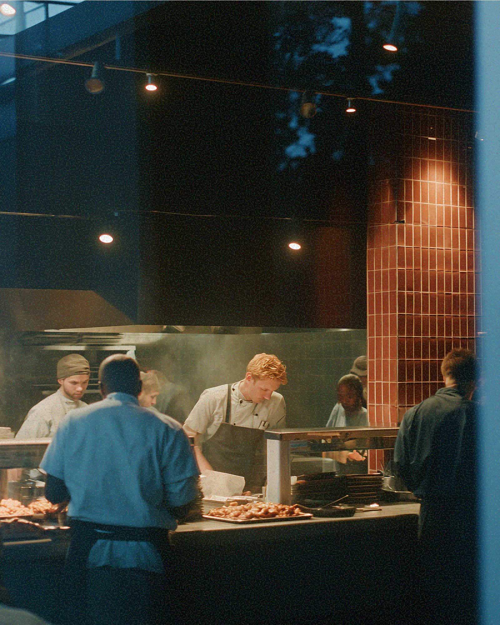 Chefs working in a busy open kitchen with trays of food and warm overhead lighting