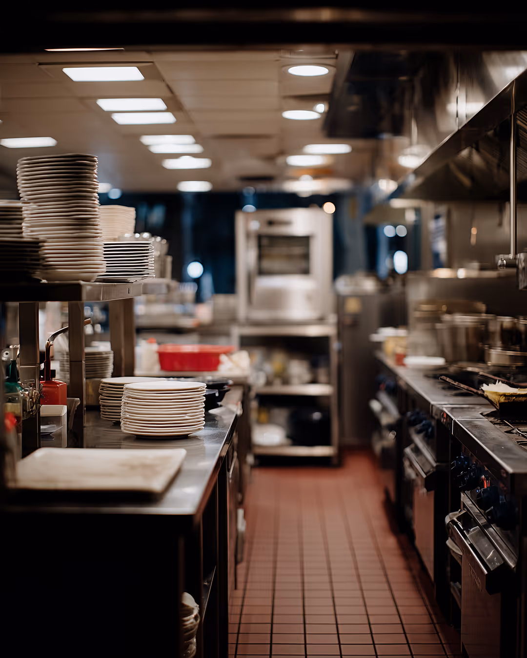 Empty commercial restaurant kitchen with stacked plates and stainless steel equipment
