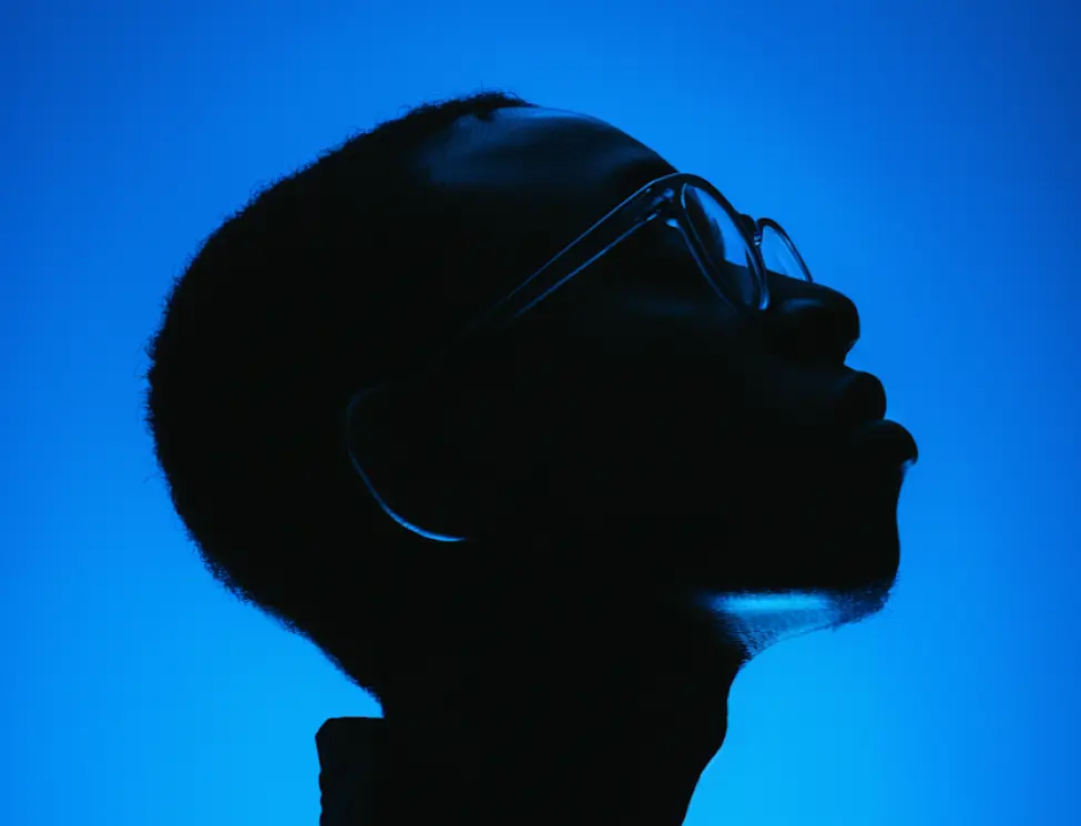 Silhouette of a person wearing glasses against a blue background, facing right with head tilted slightly upward.