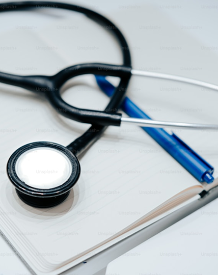 Svart stetoskop og blå penn hviler på en åpen notatbok med blanke sider.