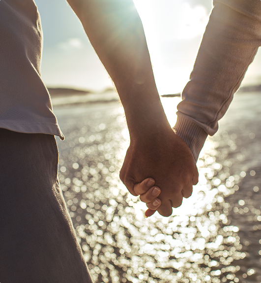 To mennesker som holder hender foran havet med solnedgang