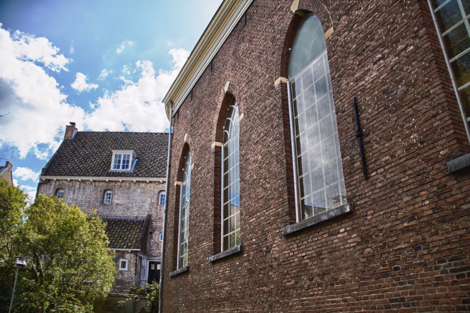Oude bakstenen gebouw met hoge boogvensters onder een blauwe lucht met wolken.