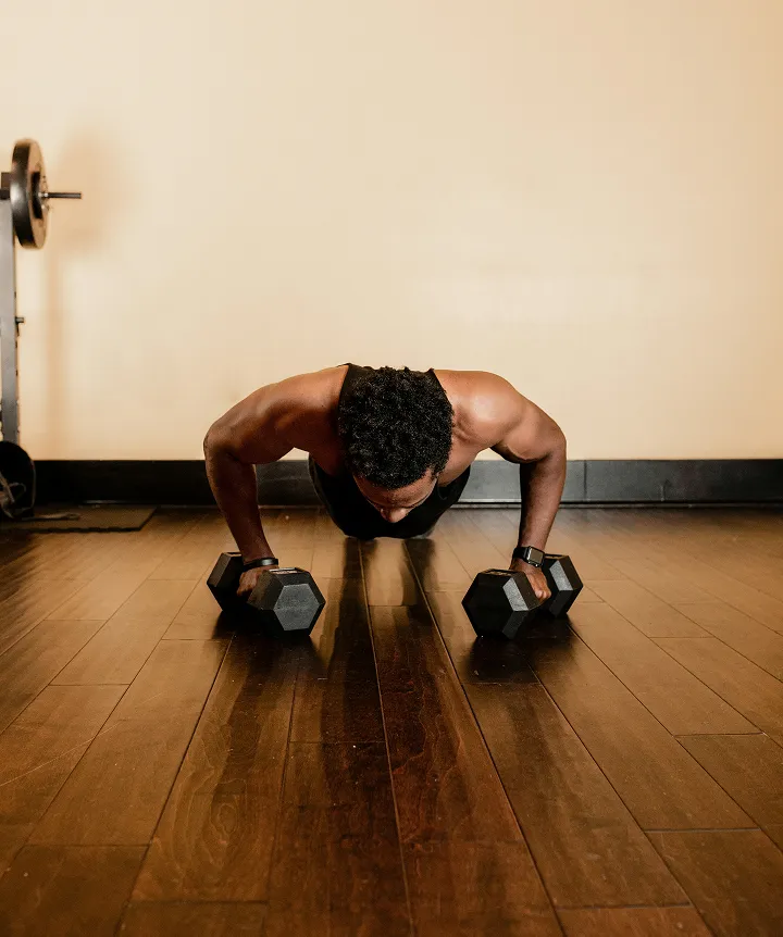 A man performs push-ups using hex dumbbells on a polished wooden floor.
