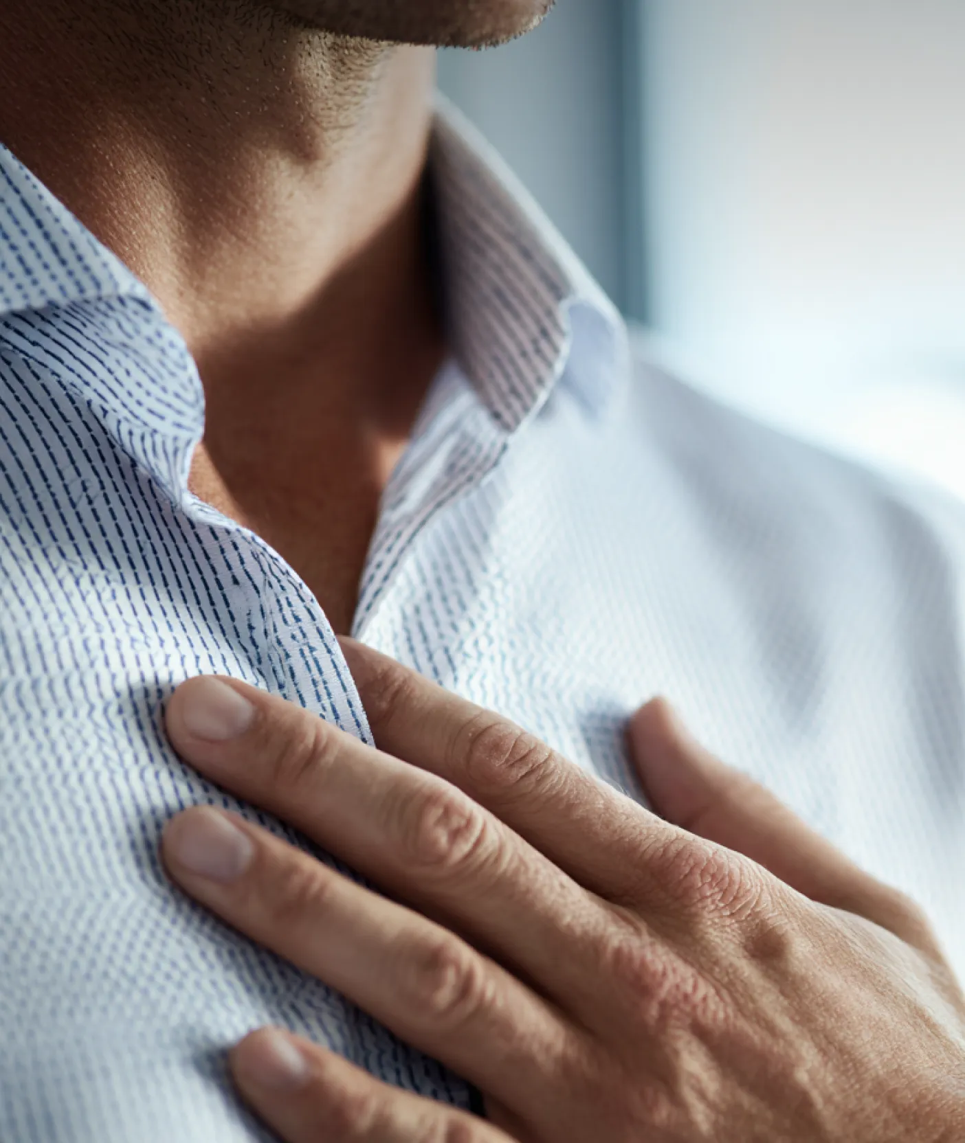 A close-up shot of a hand resting on a person's chest over a light blue striped shirt.
