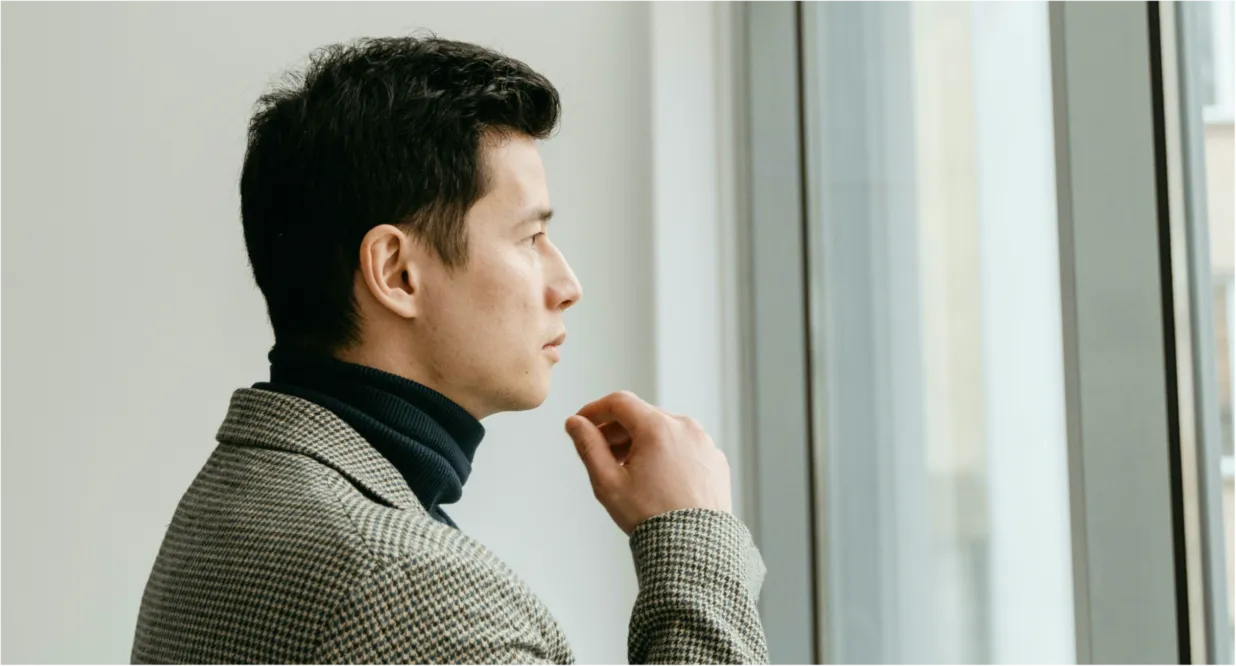A man in a checkered blazer and turtleneck looks out a large window.