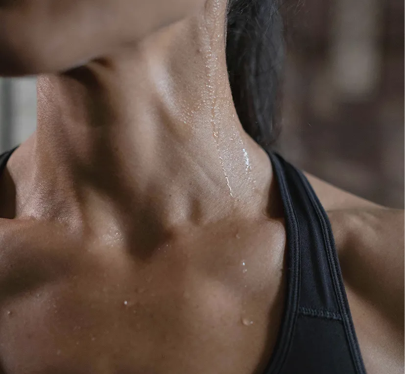 A close-up of a person's neck and collarbone covered in beads of sweat.