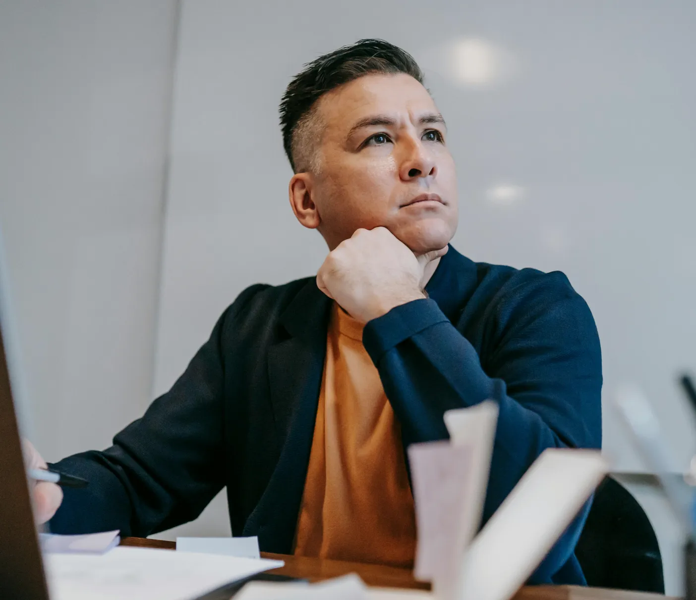 A man sits at a desk with a pensive expression, resting his chin on his hand.