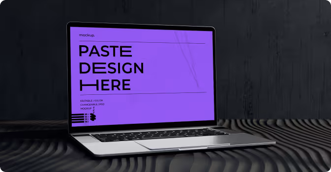 Laptop with a purple screen displaying the text 'PASTE DESIGN HERE' on a dark textured surface.