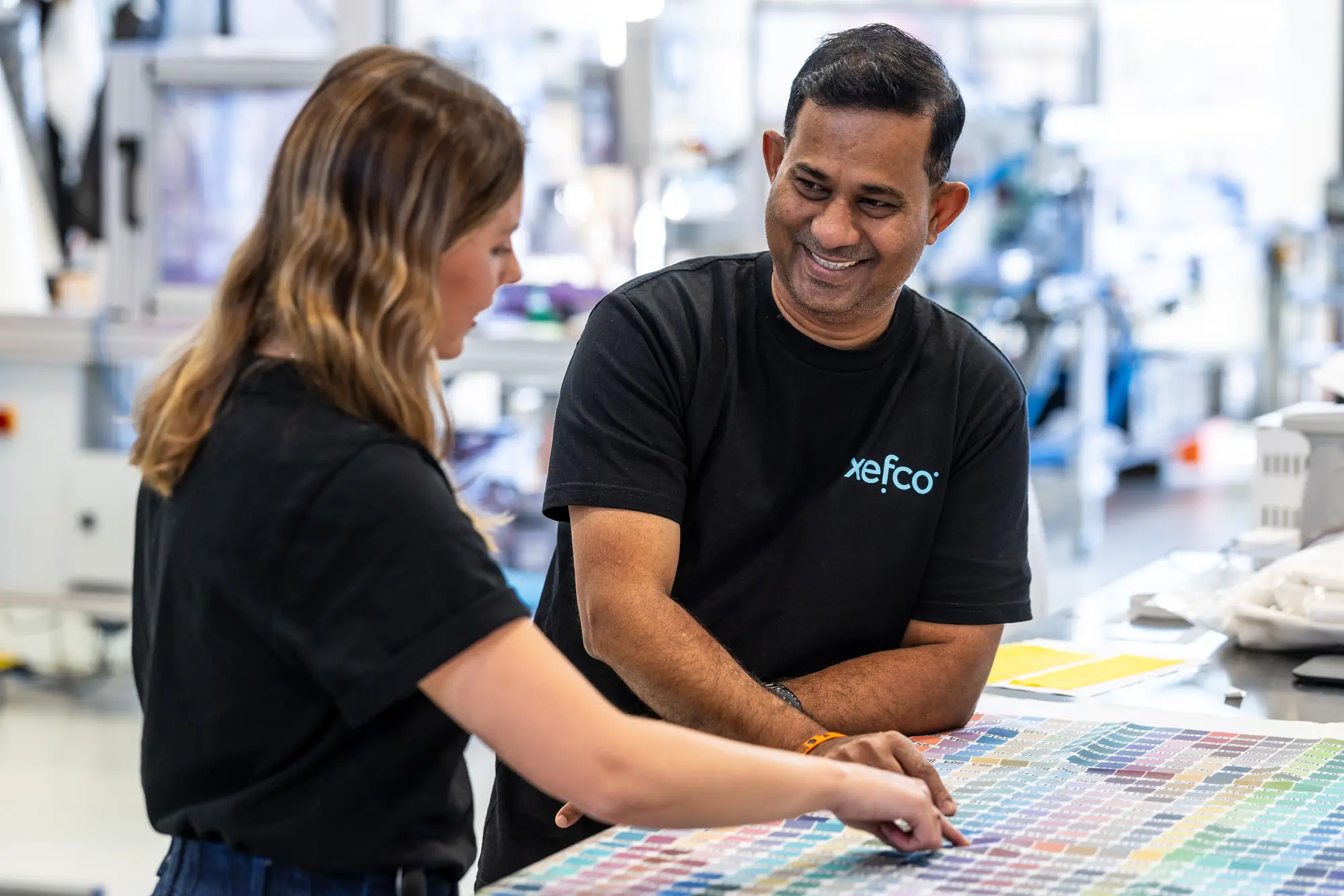 Two Xefco colourists comparing dyed fabric swatches against a colour chart