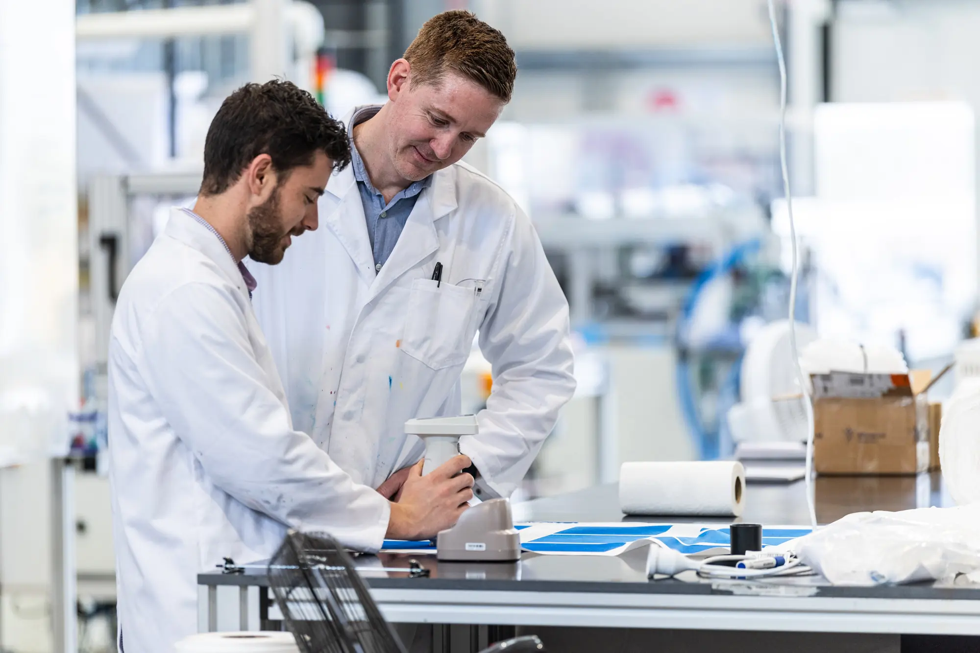 Two Xefco technicians measuring colour on finished fabric with a spectrophotometer