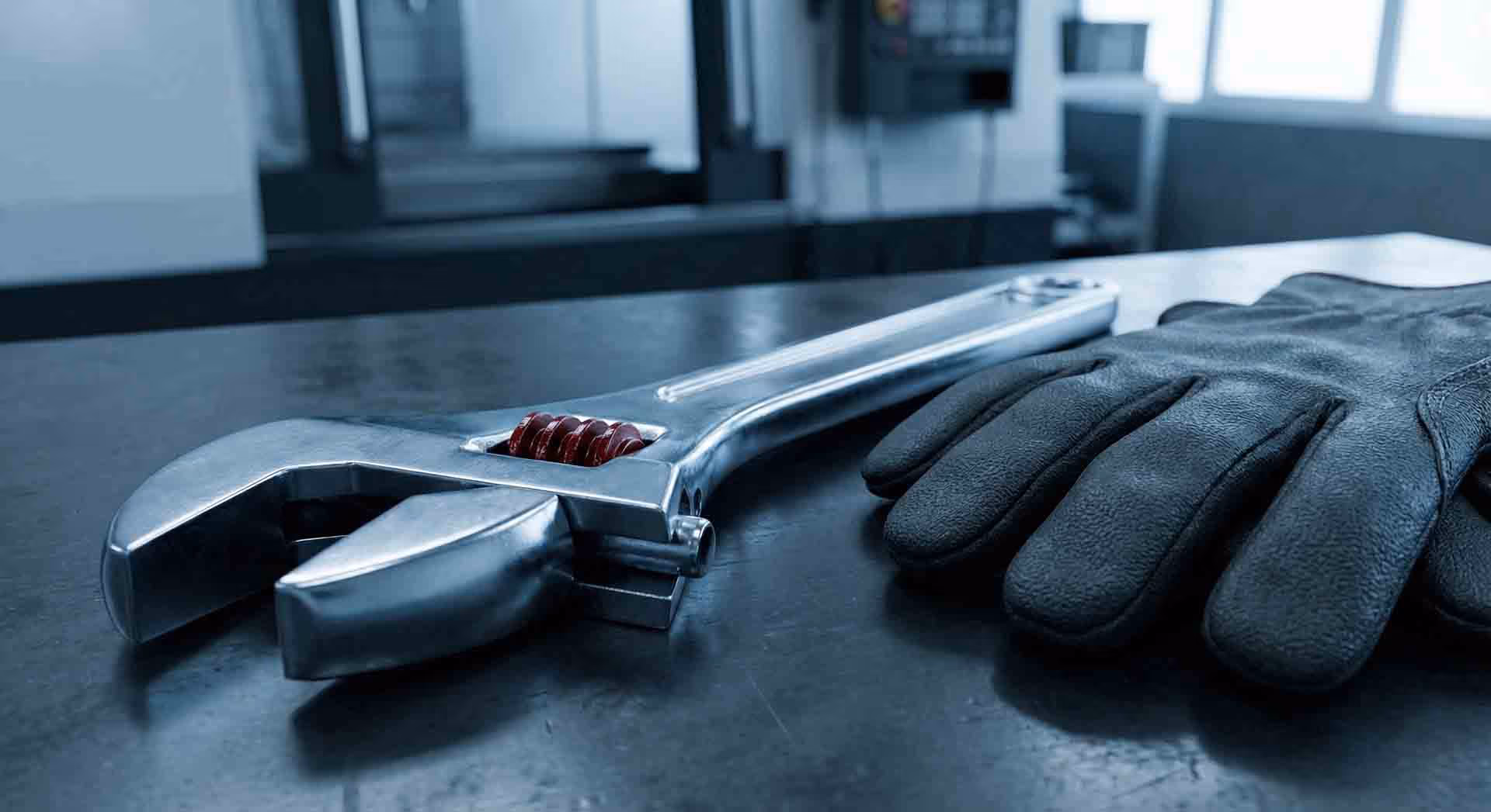 Francouzský klíč a pracovní rukavice na kovovém stole.