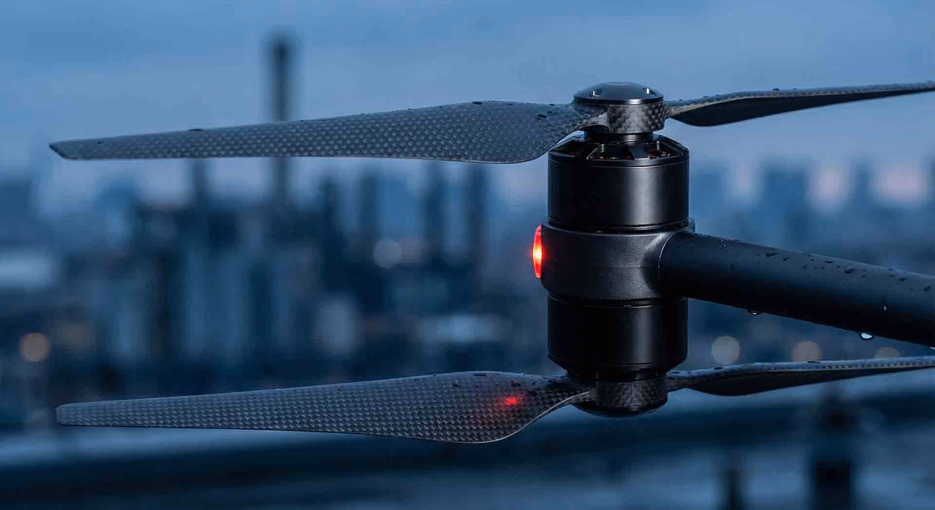 Detail vrtulí dronu s městským pozadím.