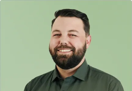 Smiling man with dark hair and beard wearing a dark green button-up shirt against a light green background.