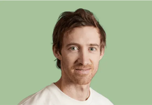 Man with short brown hair and light facial hair wearing a white shirt against a light green background.
