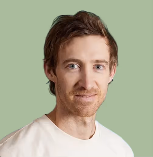Headshot of a man with light skin, short brown hair, and a light beard wearing a white shirt against a light green background.