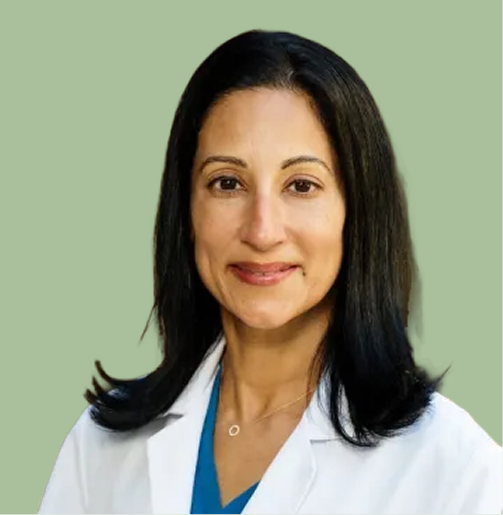 Woman with dark hair wearing a white lab coat and blue top, smiling against a green background.