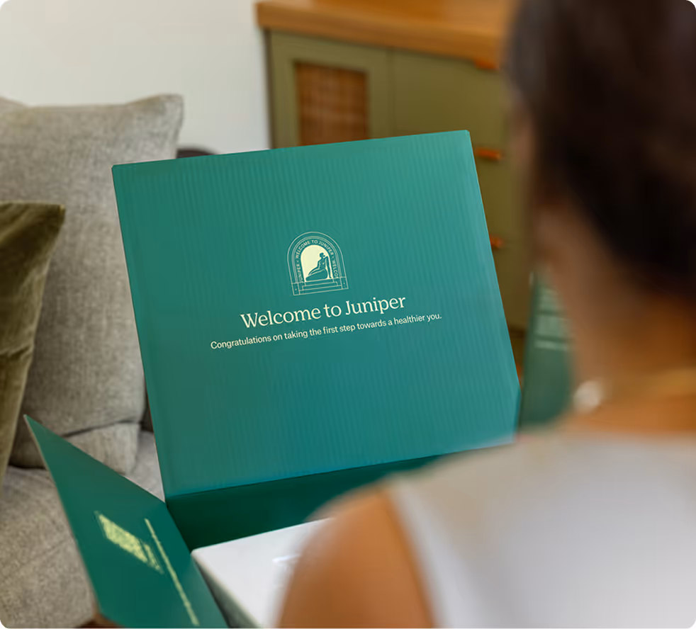 Woman holding an open green box with the text 'Welcome to Juniper' and a congratulatory message inside the lid.