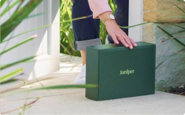 Person placing a green Juniper-branded box on a doorstep outside a house.