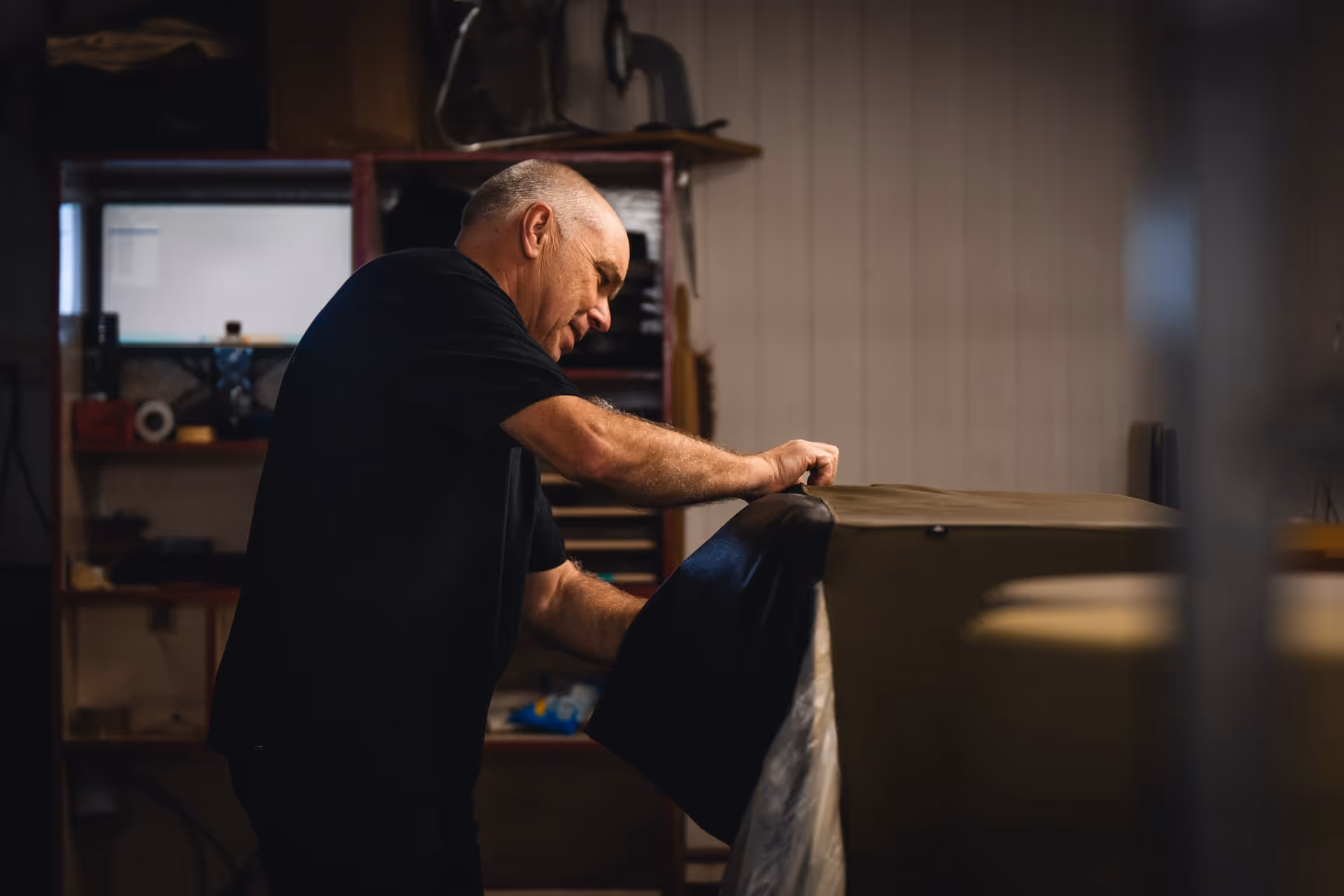 Man die in de werkplaats van Atelier Dries met bekledingsstof op een stoel werkt.