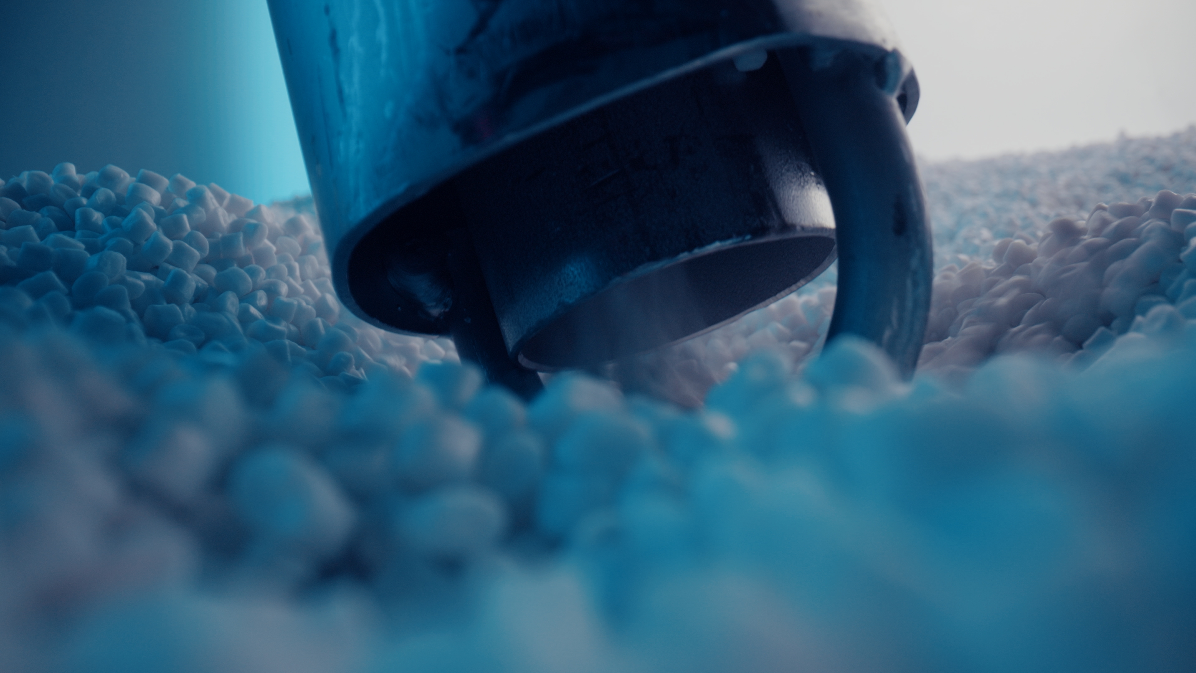 Close-up of a metal nozzle that emits whitish, slightly bluish shimmering plastic pellets.