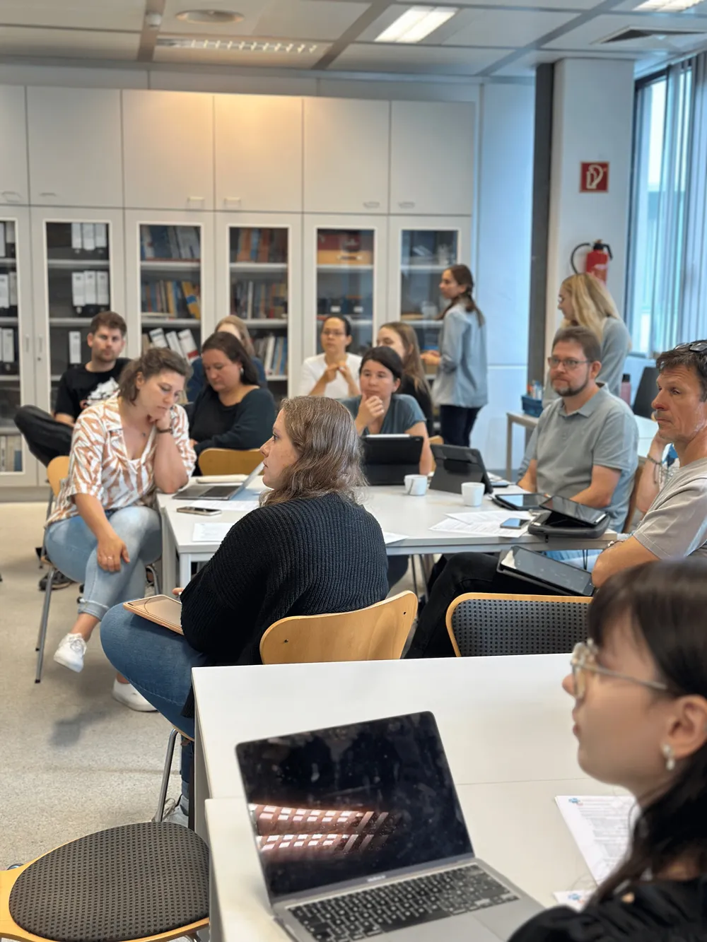 Menschen sitzen am Tischen und hoeren zu 