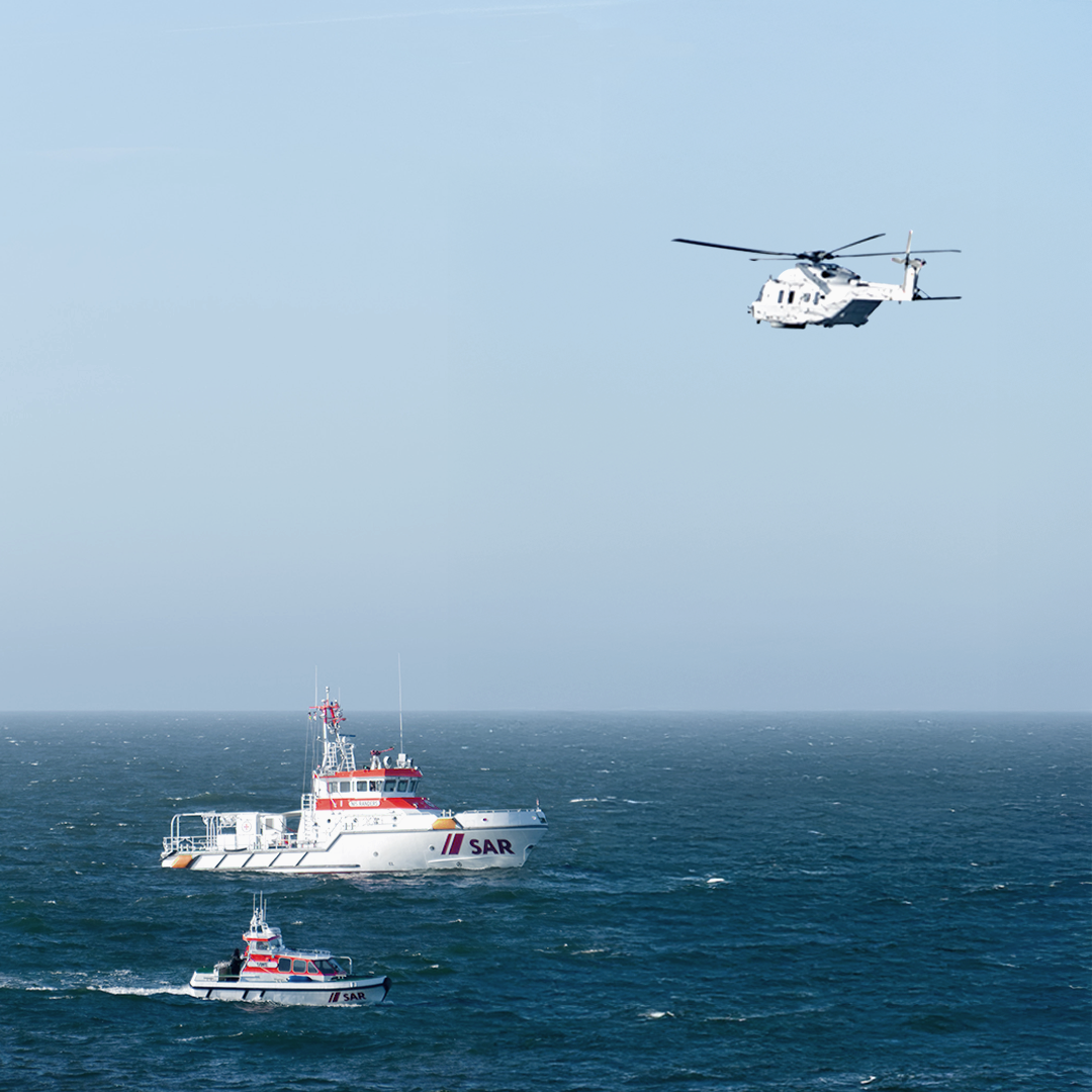 Two search and rescue boats and a helicopter conducting a training exercise at sea.
