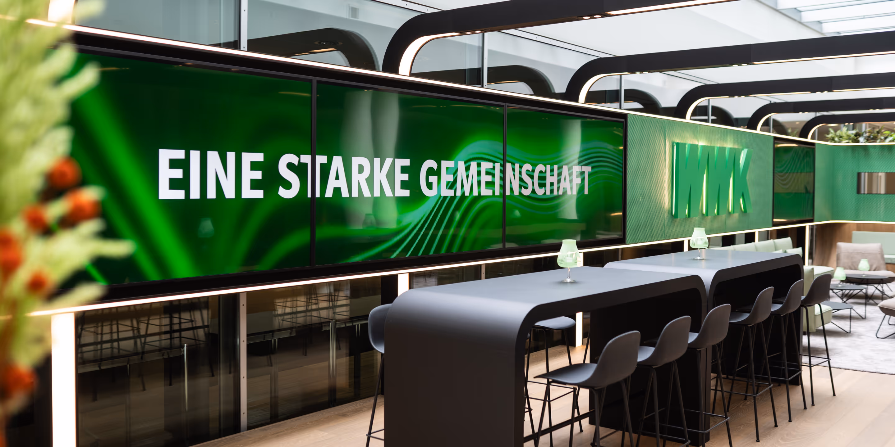 Moderner Besprechungsraum mit langen Tischen, schwarzen Stühlen und grüner Wand mit dem Schriftzug 'EINE STARKE GEMEINSCHAFT' und dem WMK-Logo.