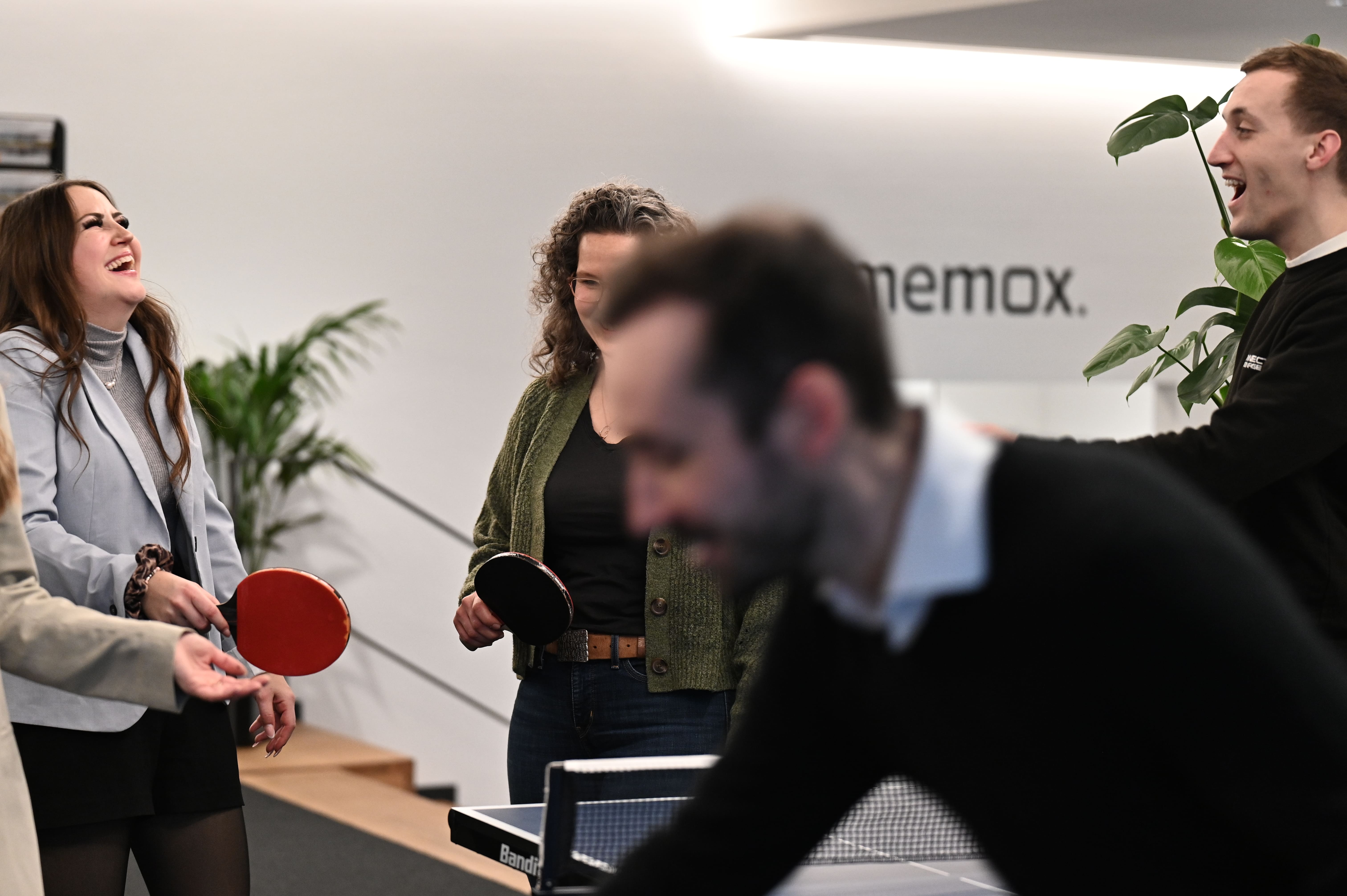 Vier Personen spielen und lachen beim Tischtennisspiel in einem modernen Büro.